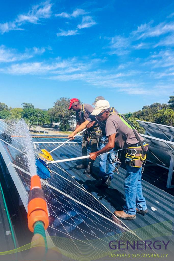 People on rooftop cleaning solar panels with hose pipe spraying water in the foreground